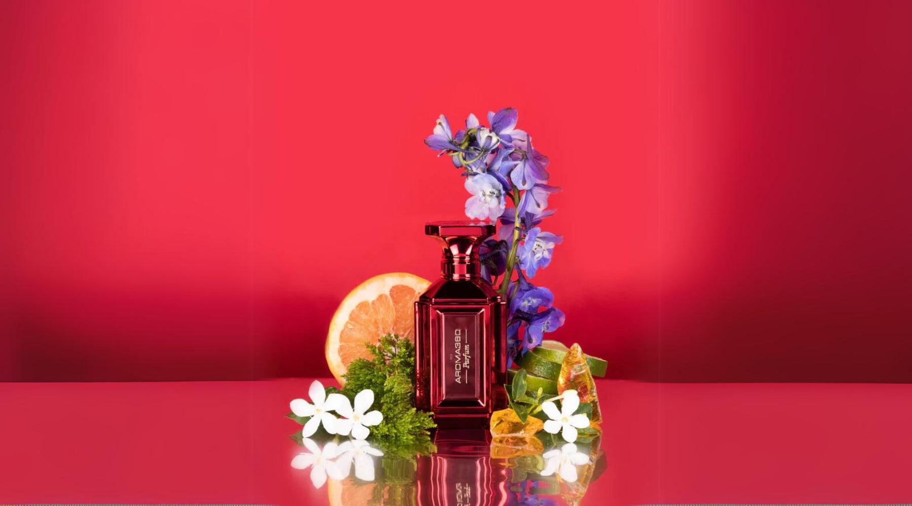 Aroma360's Red perfume surrounded by a grapefruit, bergamot, and jasmine against a red backdrop.